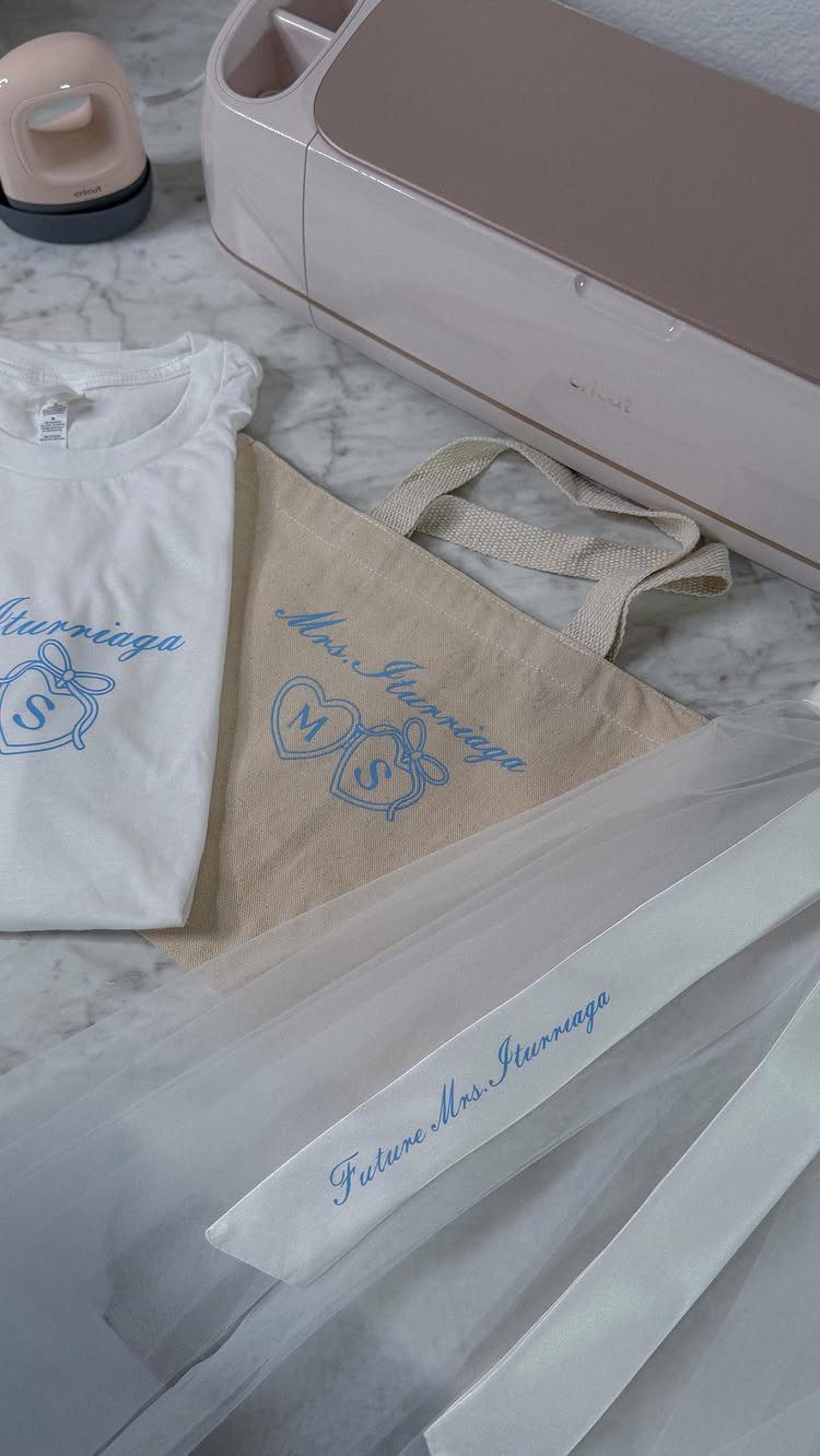 Personalized white t-shirt, beige tote bag, and garment bag with blue bridal lettering.