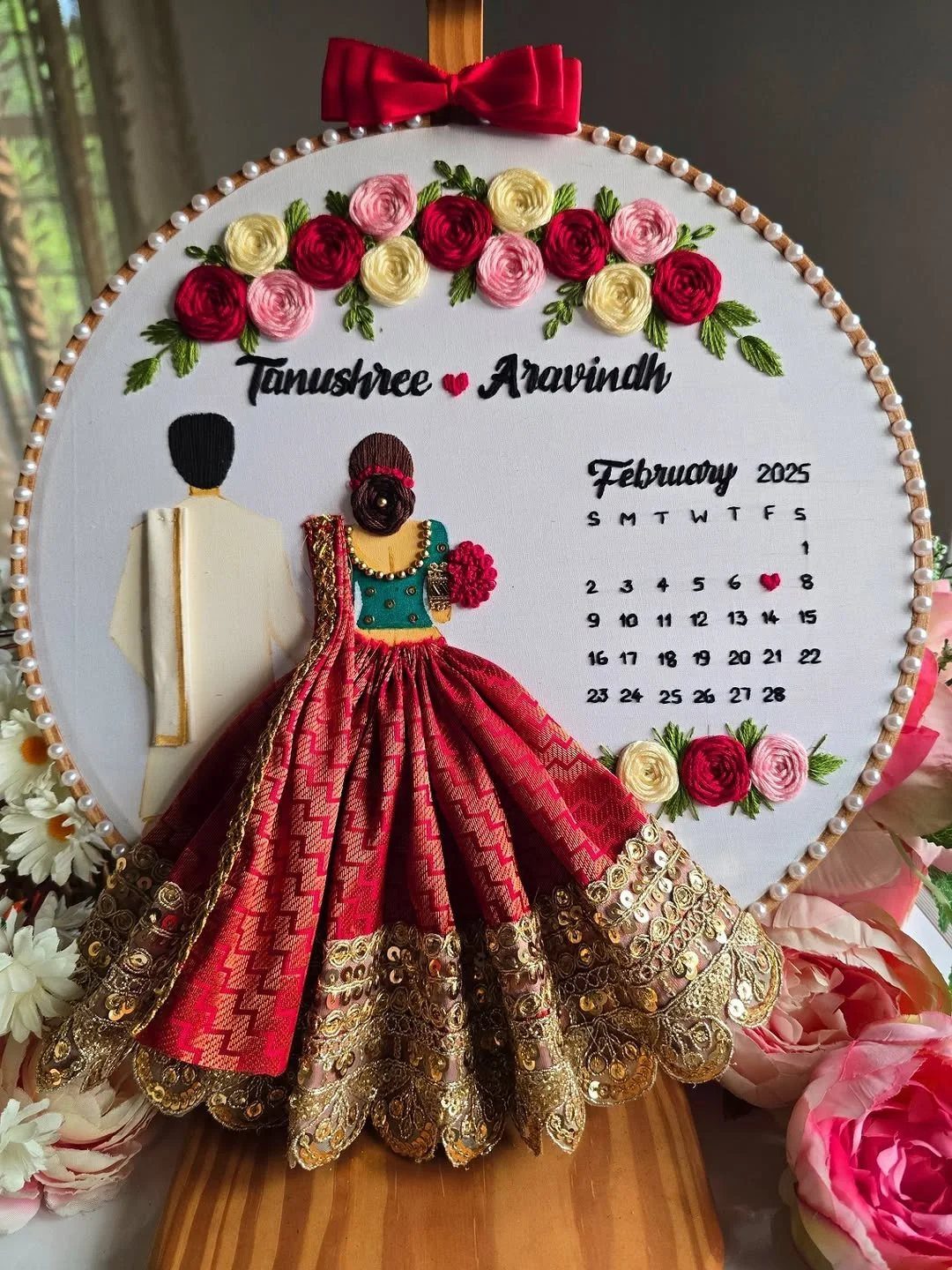 Embroidery hoop art featuring a couple in traditional Indian wedding clothes and a calendar.