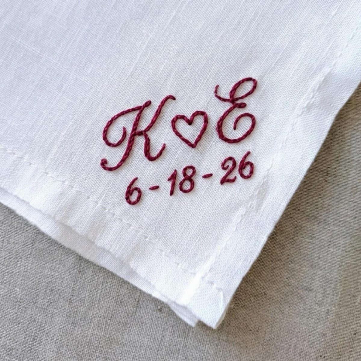 White linen handkerchief with red embroidered initials, a heart, and a wedding date.