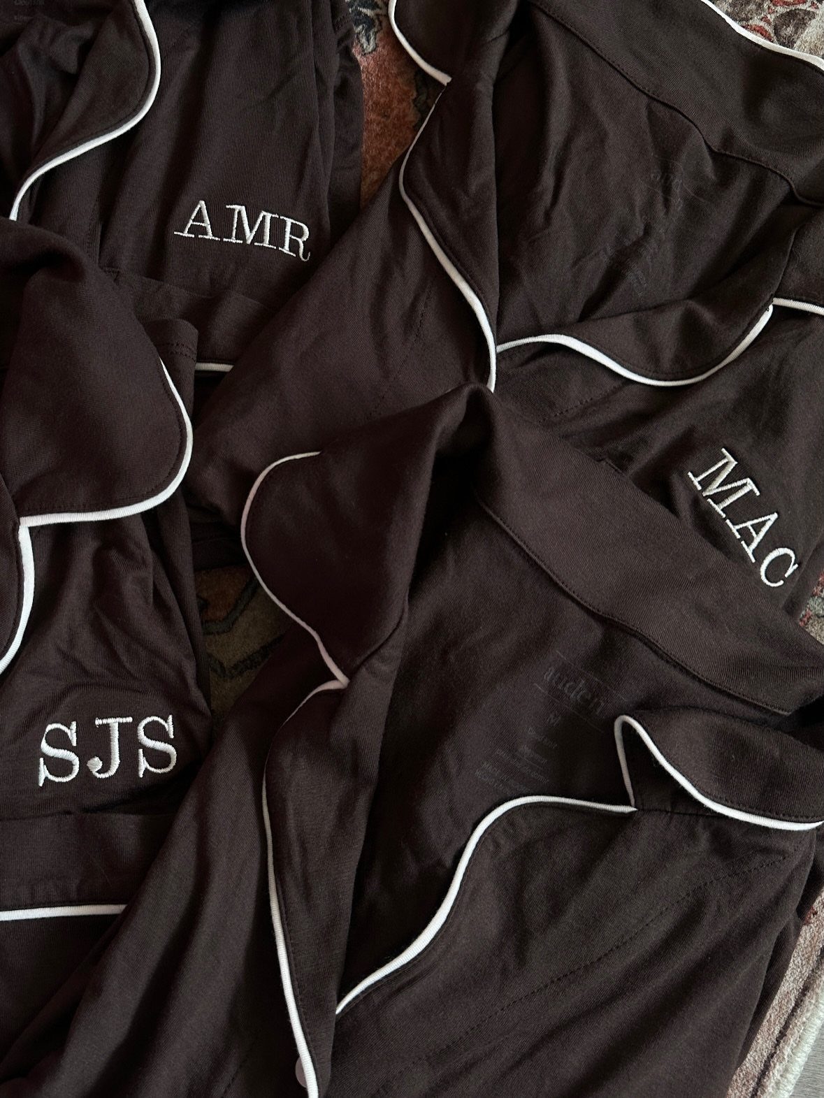 Black satin pajamas with white piping and embroidered initials on the pockets.