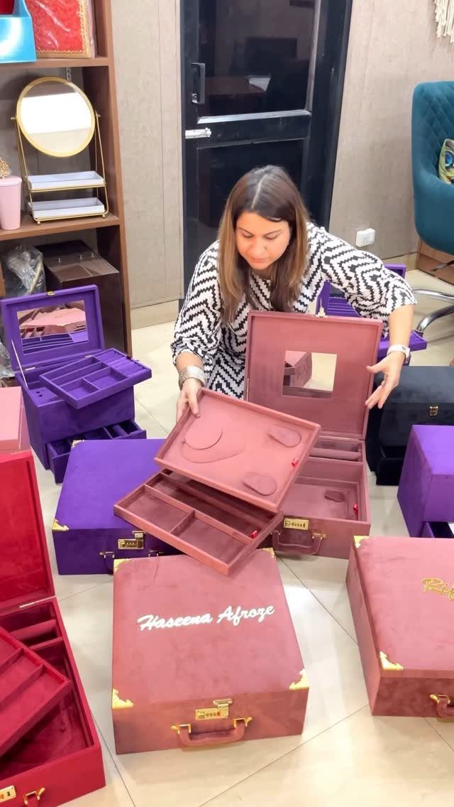 Woman standing with large red and purple velvet jewelry trunks with personalized lids.