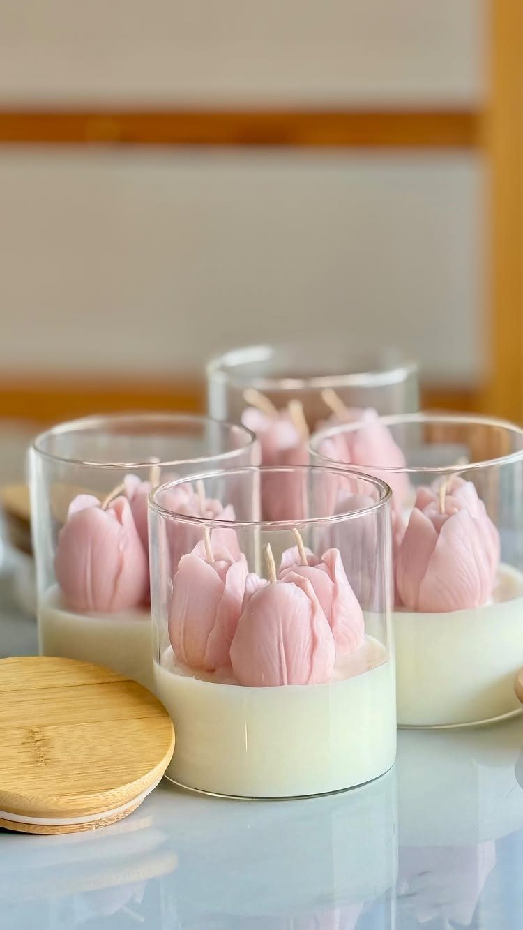 Pink tulip-shaped candles in small glass jars with a wooden lid nearby.