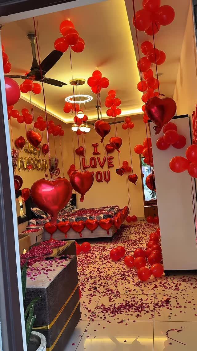 Romantic bedroom decorated with red heart balloons and rose petals on the floor.