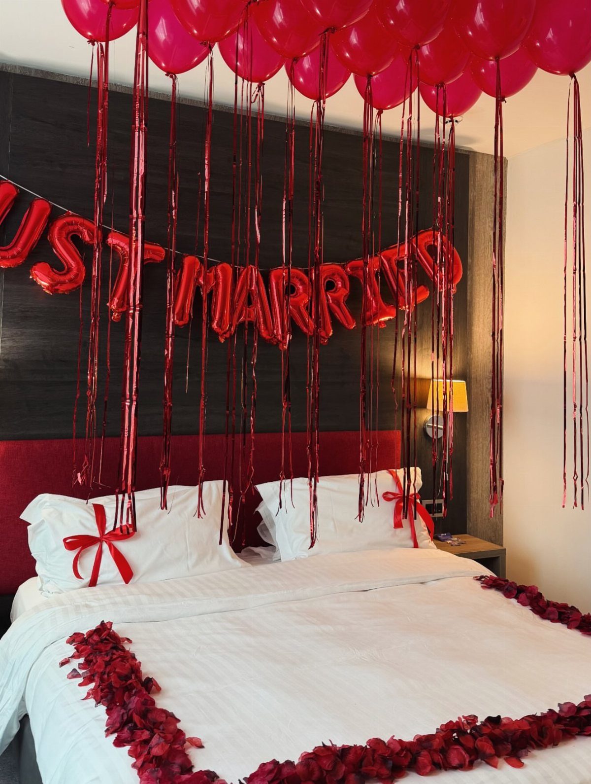 Red foil Just Married balloons and red balloons over a bed with rose petals.