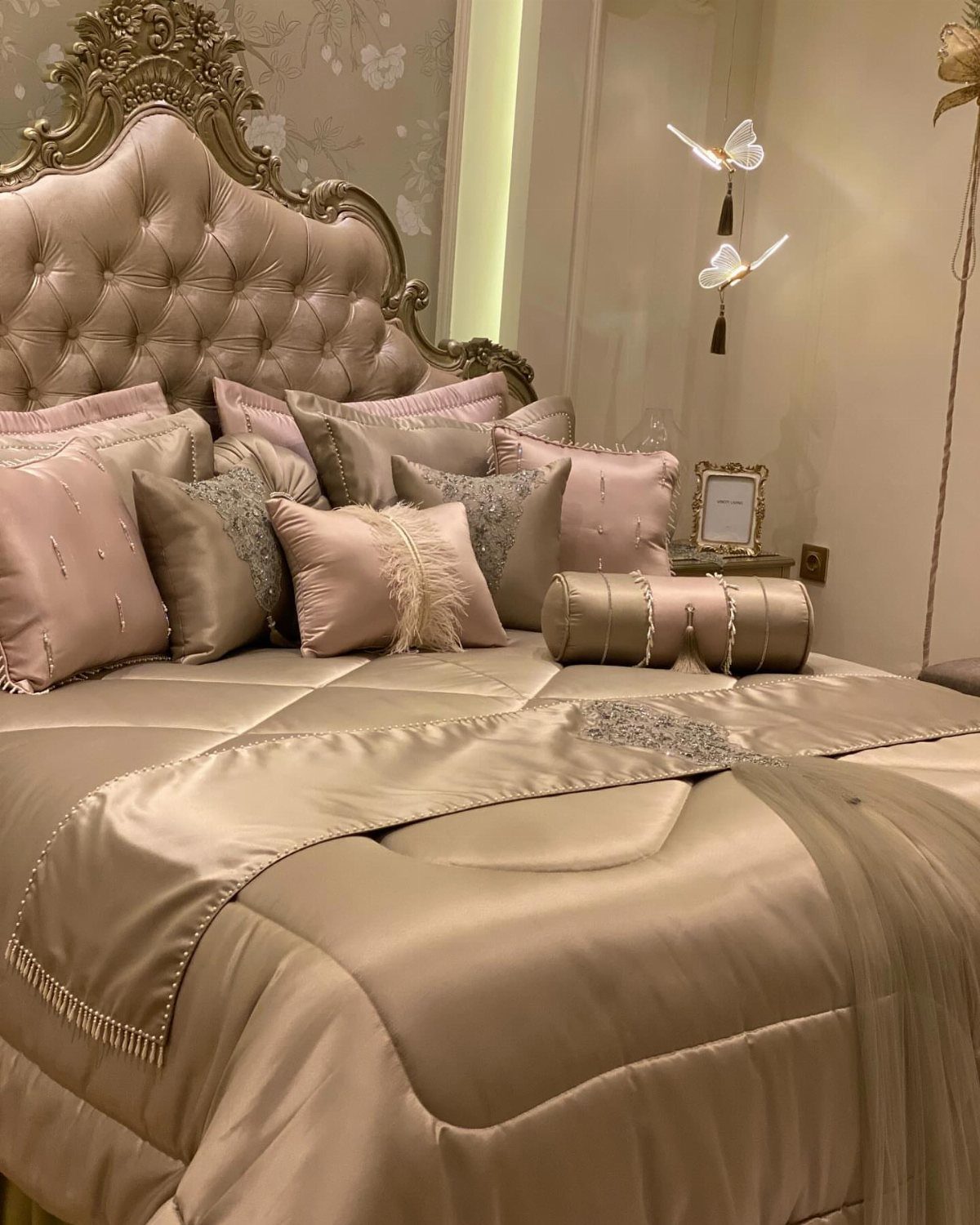Luxurious champagne satin bedding with plush pillows and an ornate gold headboard.