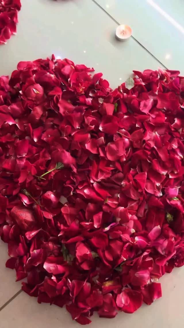 Red rose petals arranged in a heart shape on a light tiled floor.