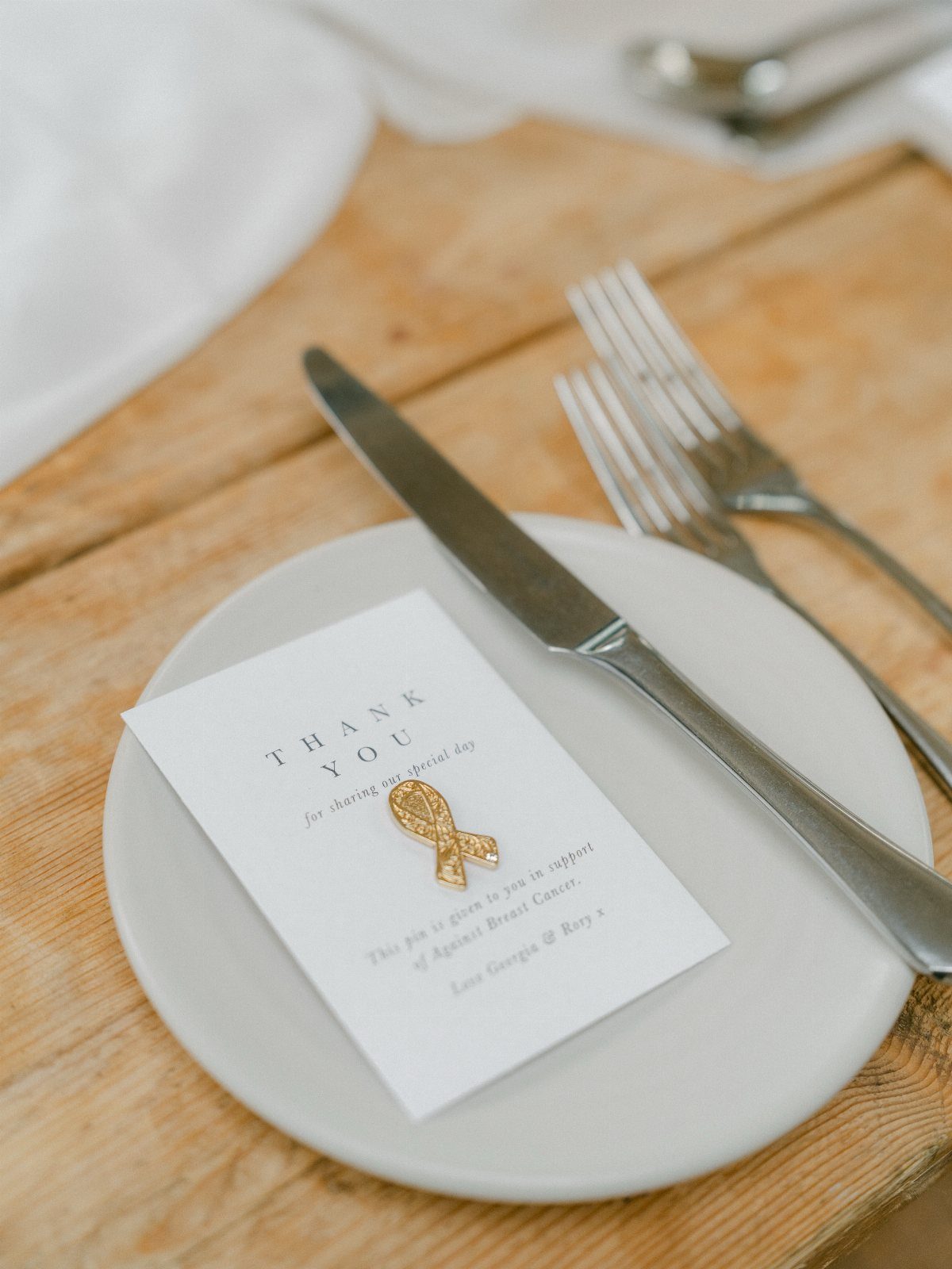 Thank you card with gold ribbon pin on a white plate at wedding table