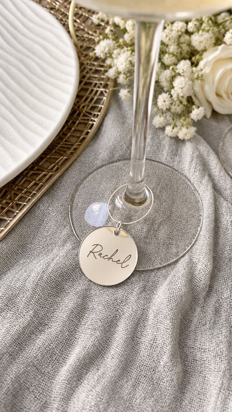 Gold circular drink charm engraved with Rachel attached to a champagne glass stem