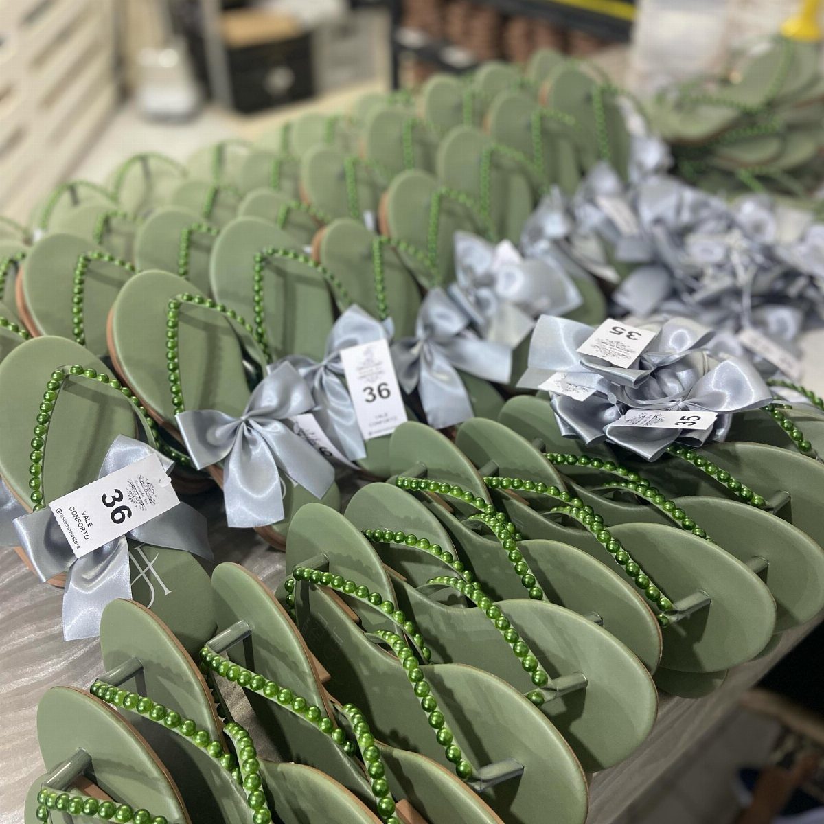 Sage green flip-flops with beaded straps and silver satin bows on display.