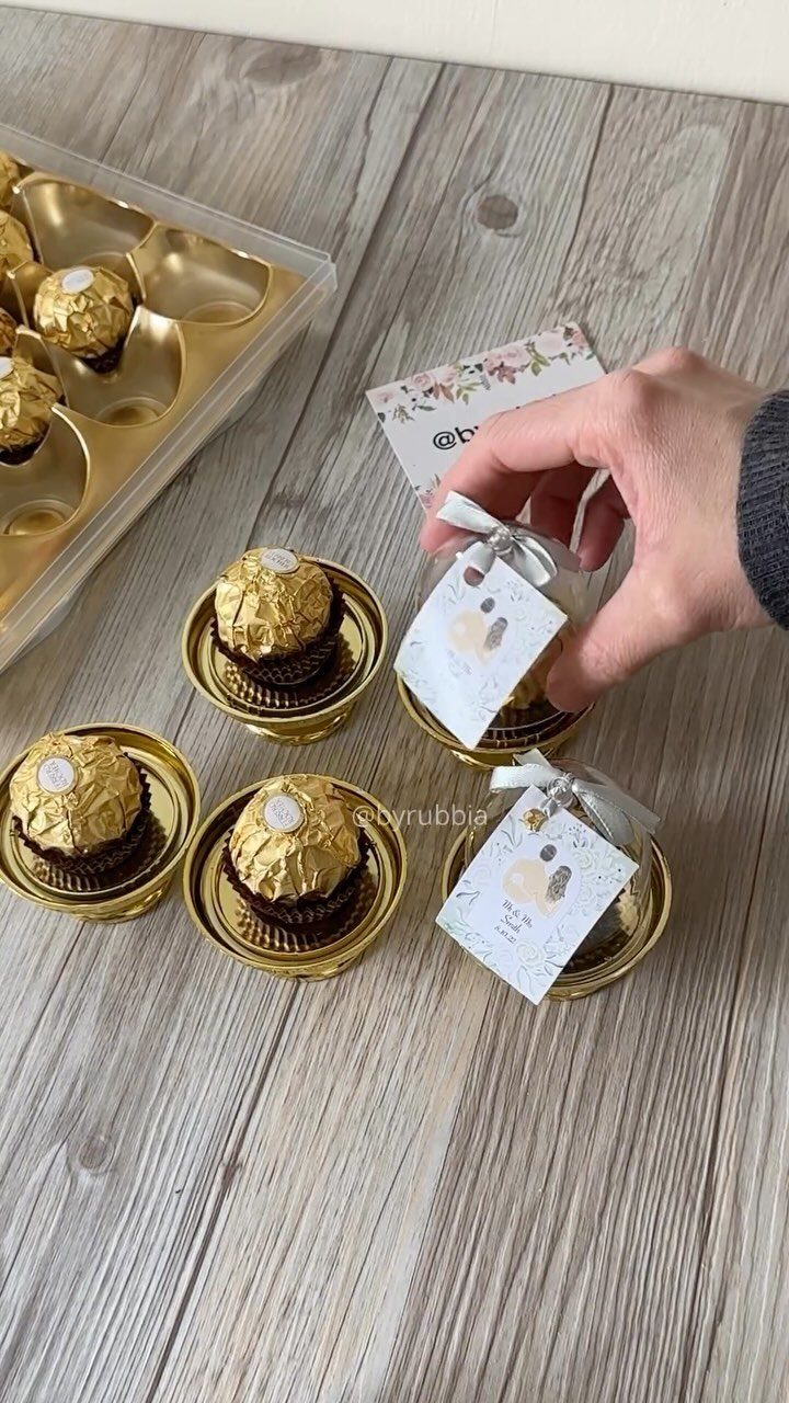 Gold-wrapped chocolate truffles in gold cups with white ribbons and tags on wood.