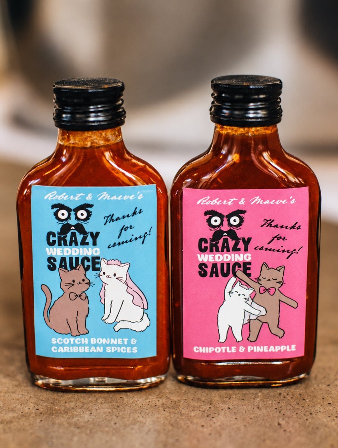 Two mini bottles of wedding hot sauce with cute cat labels and black caps.