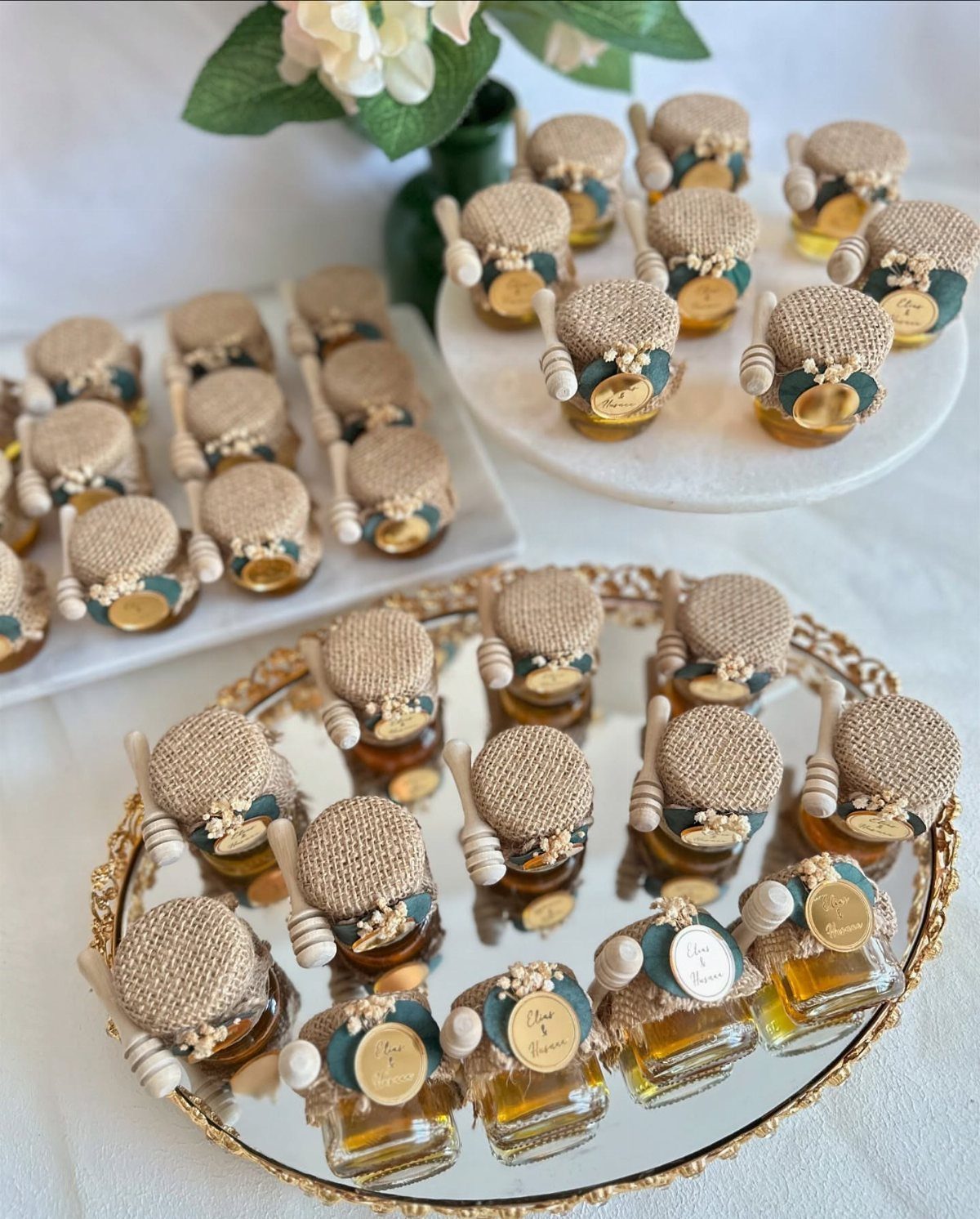 Small honey jars with burlap lids and wooden dippers on mirrored trays.