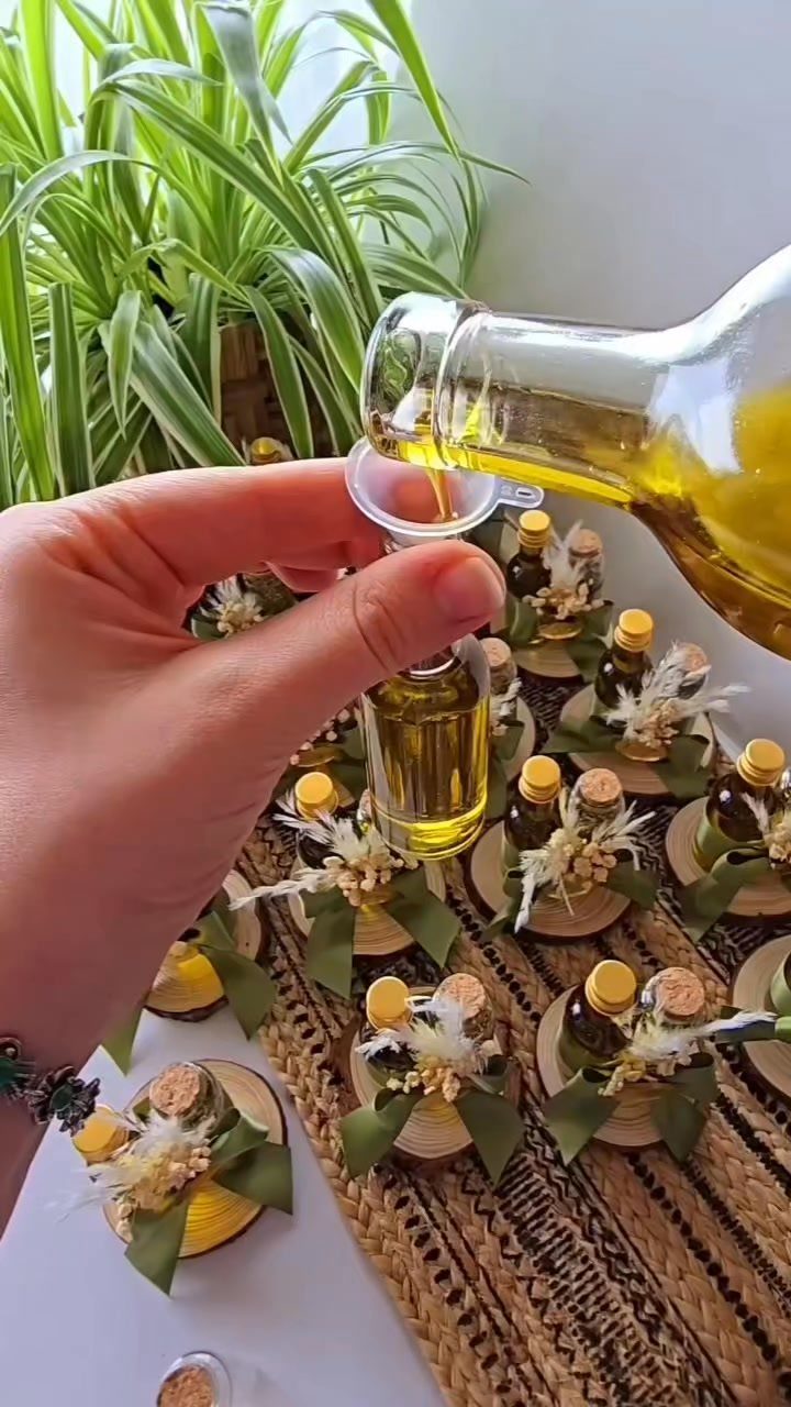 Hand pouring golden oil into small decorative glass bottles for wedding party favors.