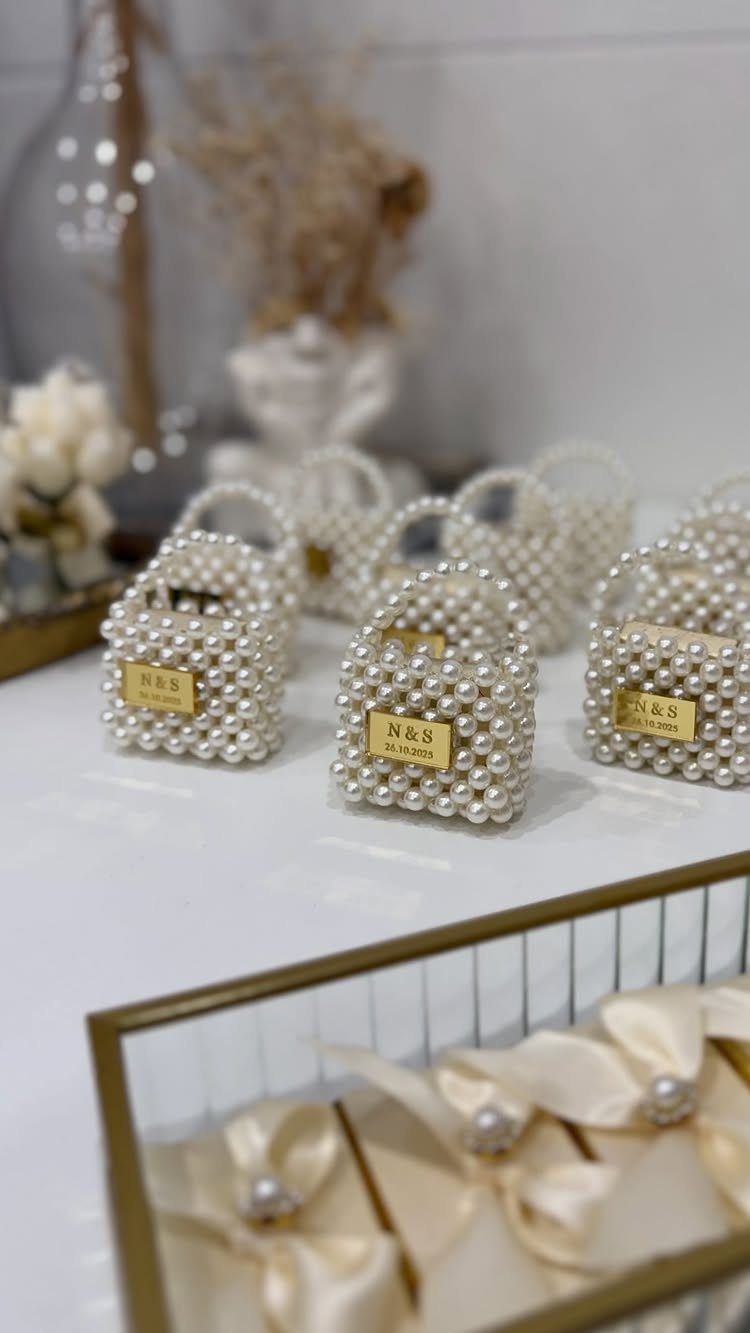 Pearl-covered handbag gift boxes with gold personalized nameplates on a white table.