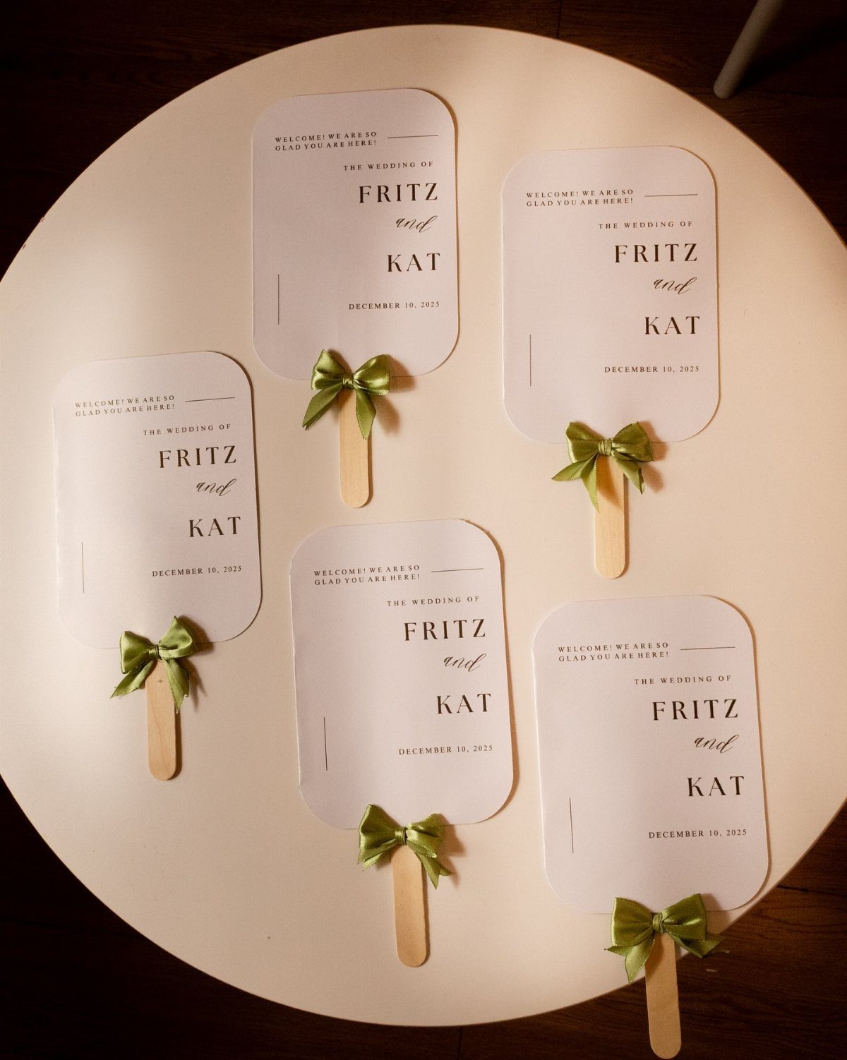 White personalized wedding fans with green ribbons and wooden handles on white background