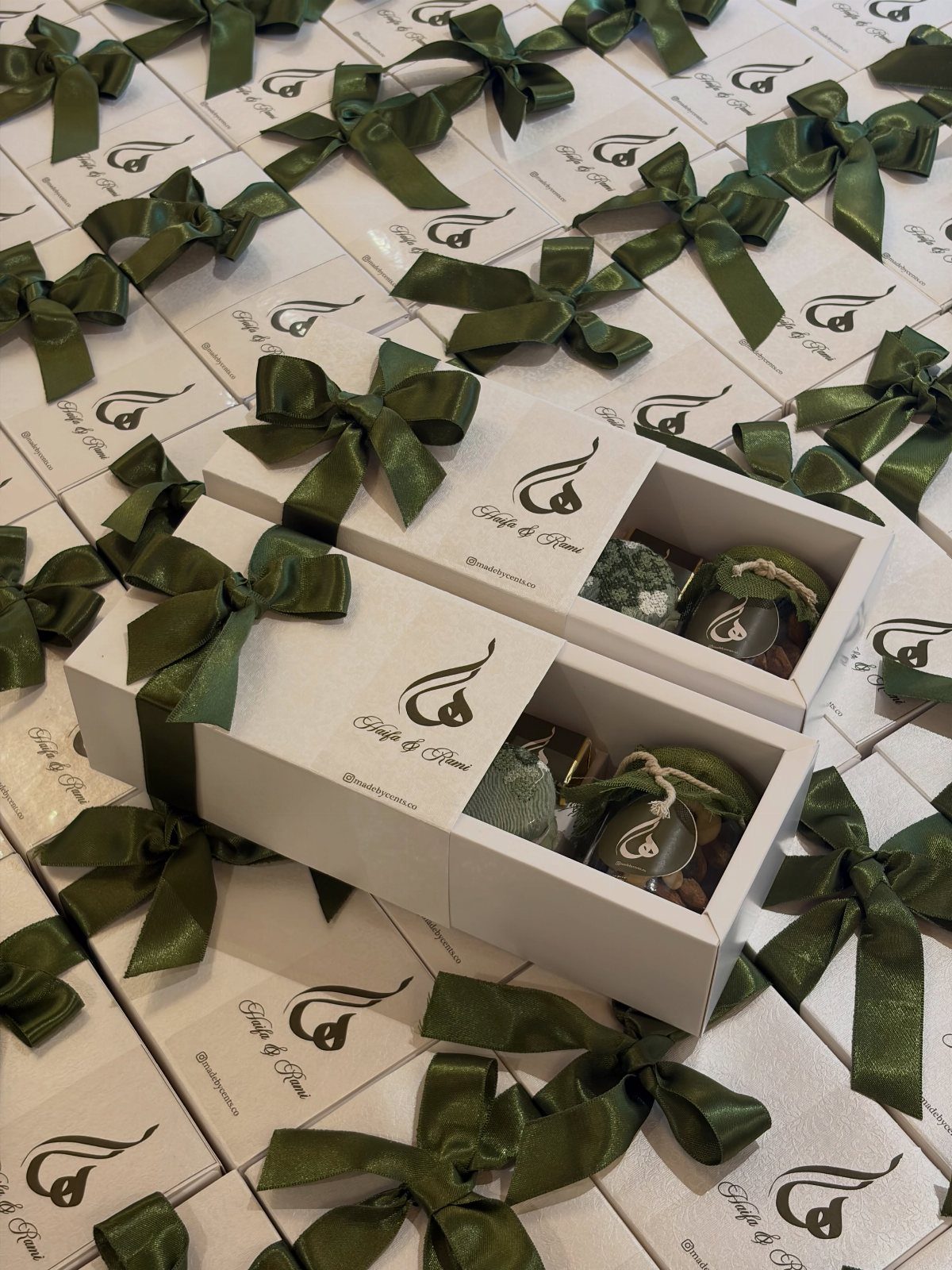 White gift boxes with green bows containing small jars of edible treats.