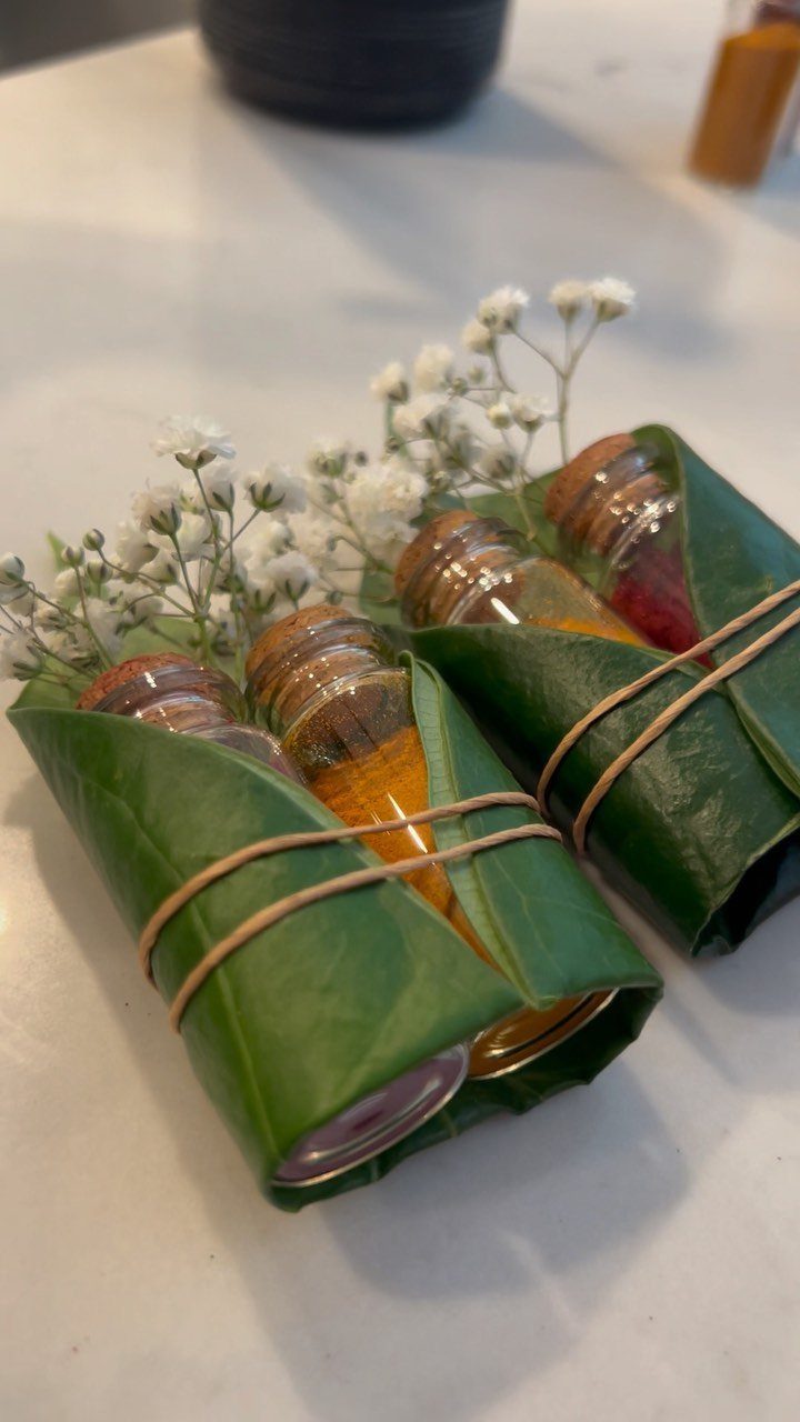 Small glass jars with yellow and red powders wrapped in green leaves and flowers.