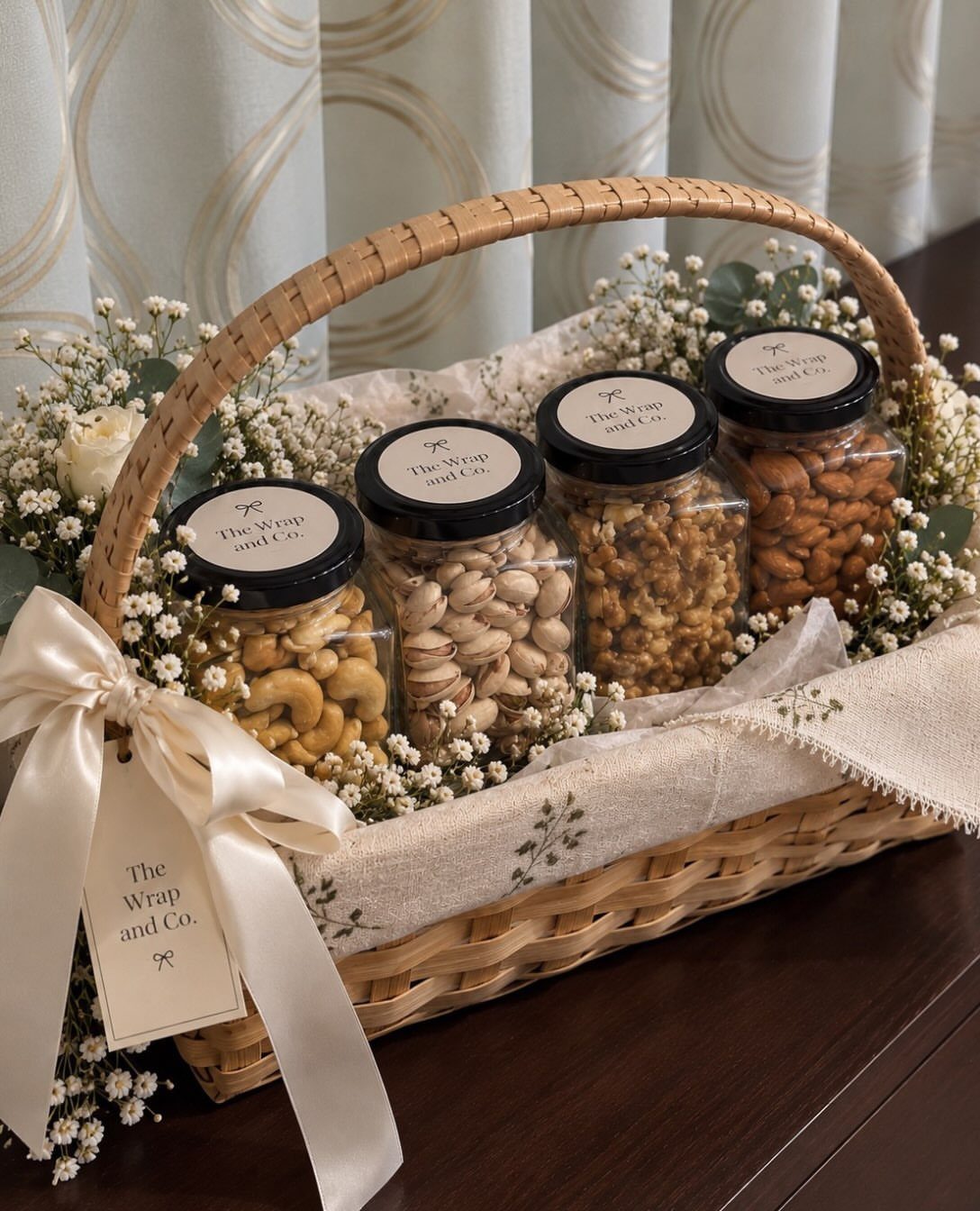 Wicker basket with four glass jars of assorted nuts and white floral decorations.