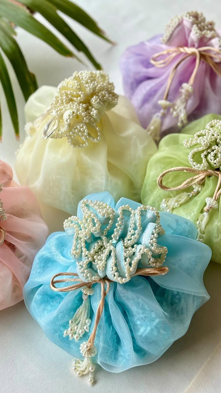 Colorful sheer potli bags with pearl embellishments and gold drawstring closures.