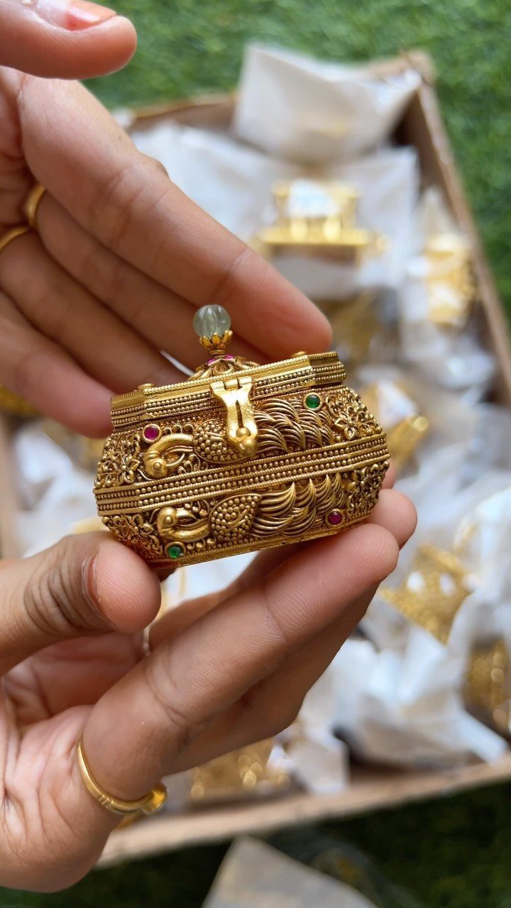 Ornate gold-colored metal box with peacock carvings held over a tray of gifts.