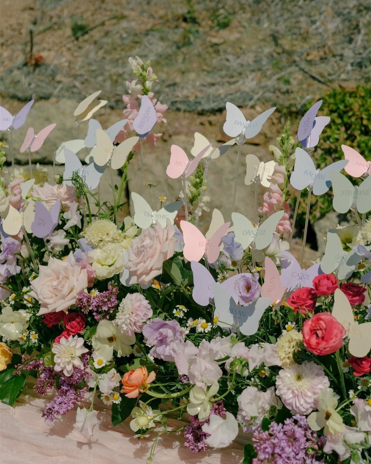 Pastel butterfly escort cards floating above a colorful floral arrangement outdoors.