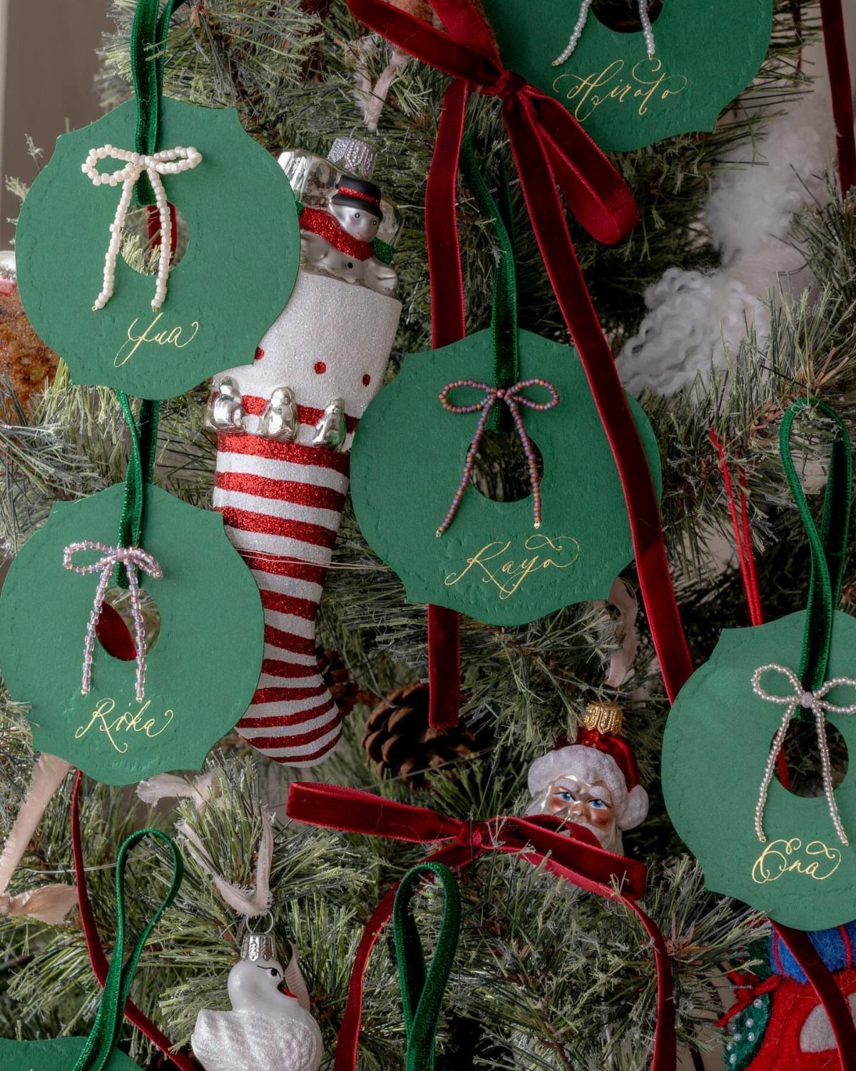 Green circular ornament place cards with gold names hanging on a Christmas tree.