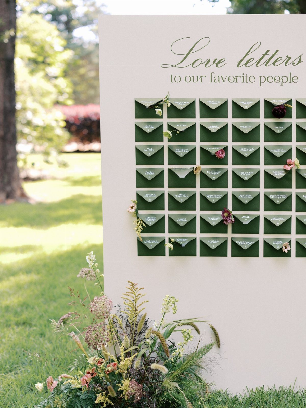 White display board with green envelopes and floral accents for wedding seating assignments.