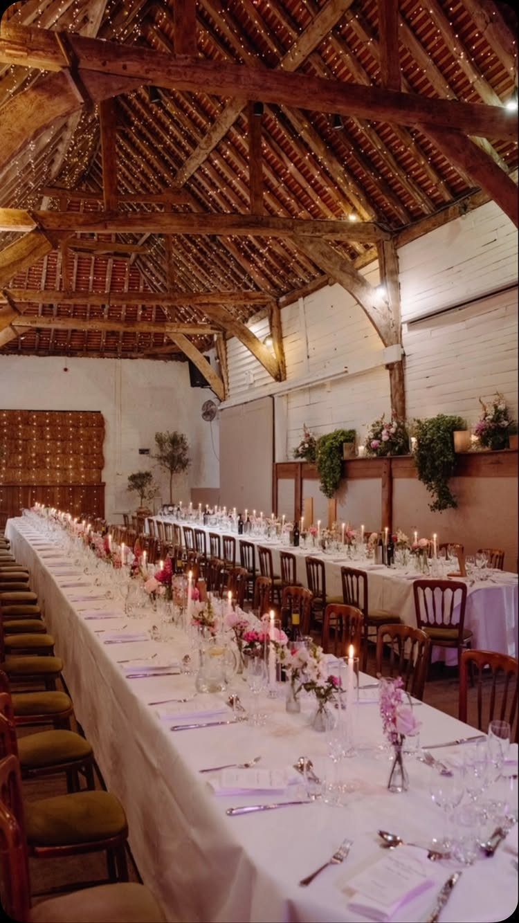 Long banquet tables with white linens and candles in a rustic wooden barn.