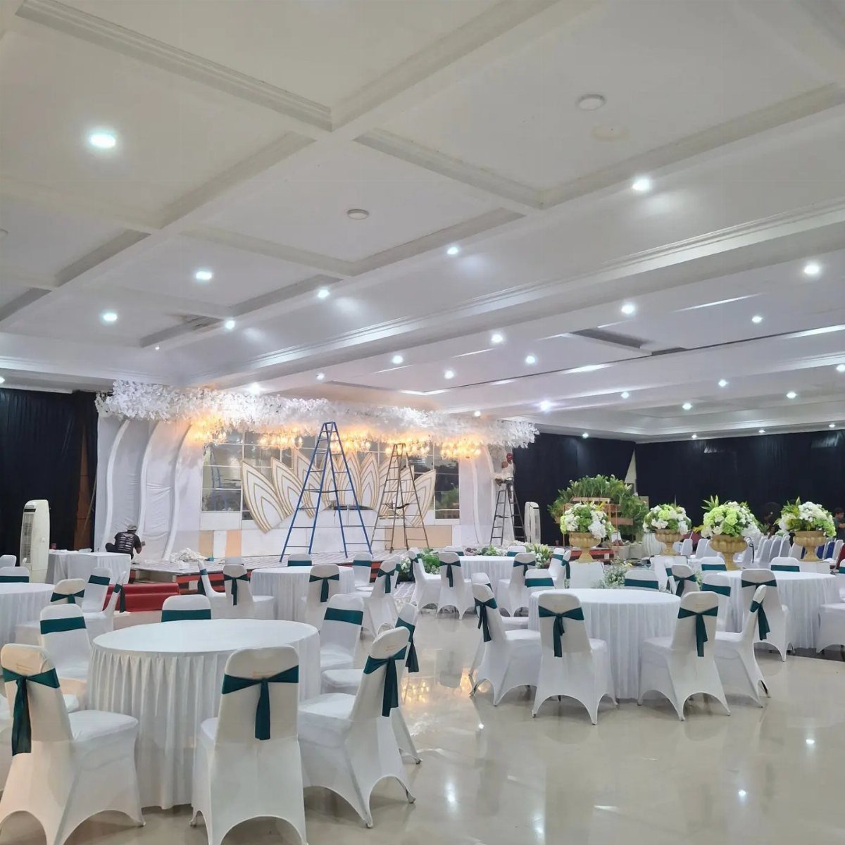 Round banquet tables with white linens and green ribbon chairs in a hall.