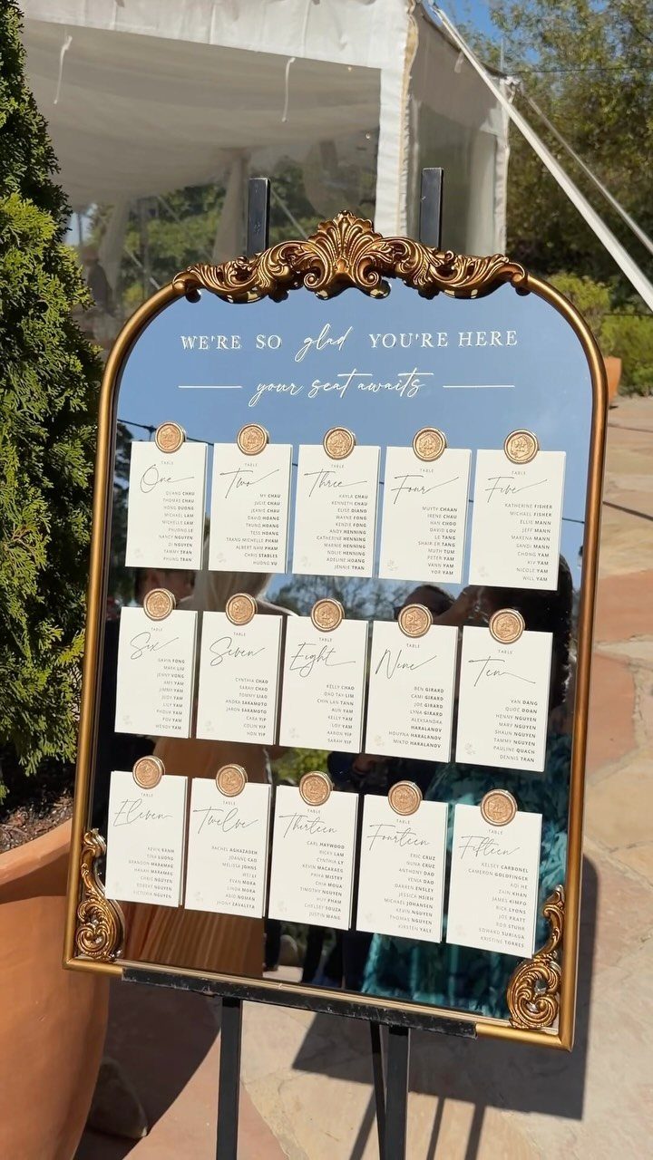 Gold-framed mirror seating chart with white guest cards pinned to the glass surface.