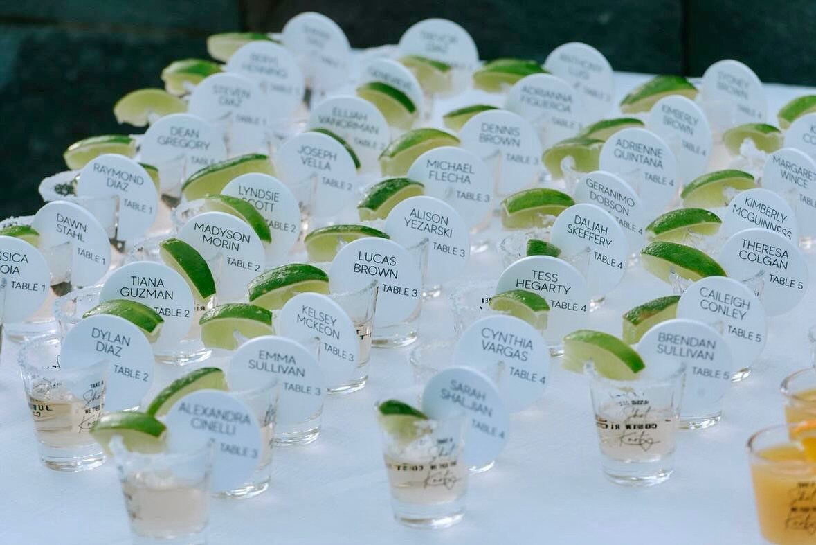 Shot glasses with lime wedges and circular name cards on a white table.