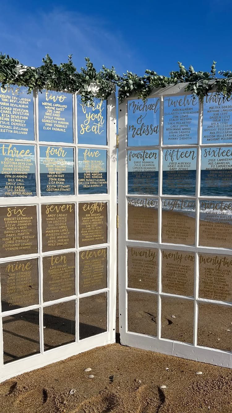 White vintage window frames used as a wedding seating chart on a sandy beach