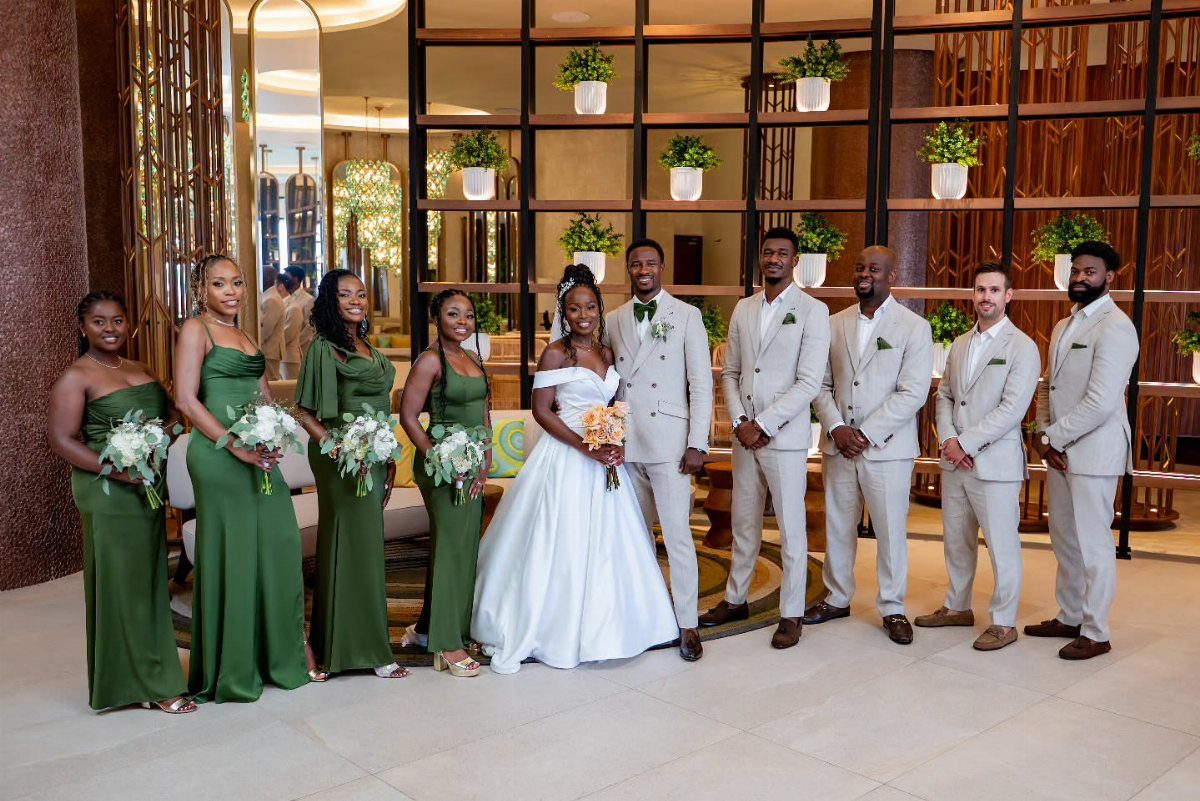 Wedding party with bridesmaids in emerald green dresses and groomsmen in beige suits.