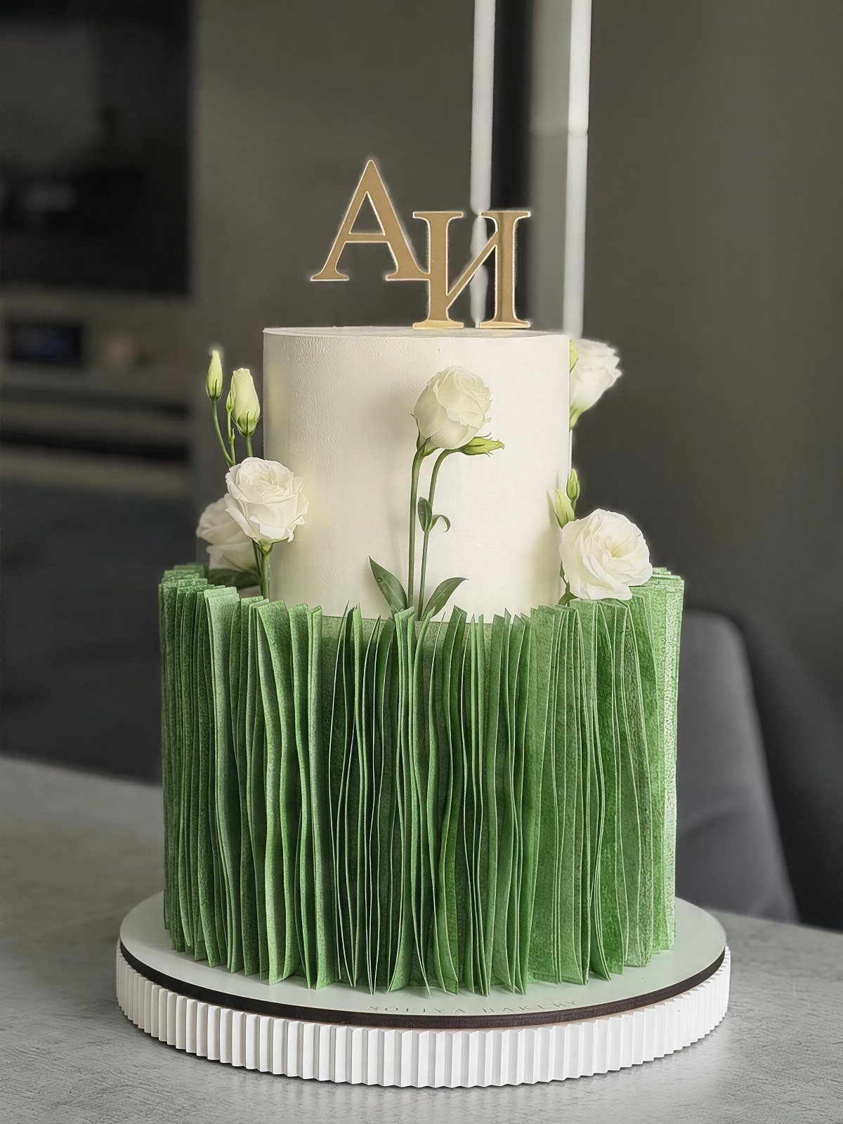 Two-tier wedding cake with a pleated green base, white top, and gold topper.