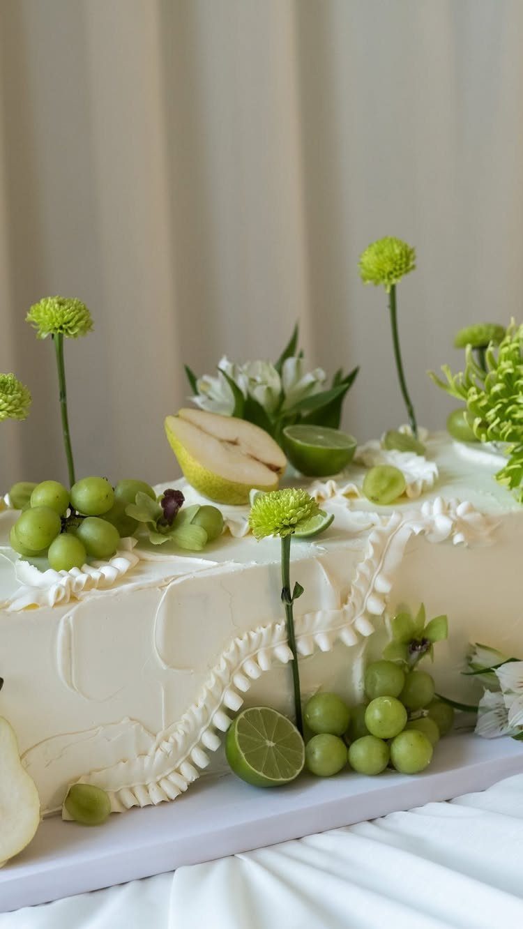 White frosted cake decorated with green grapes, lime slices, and small green flowers.