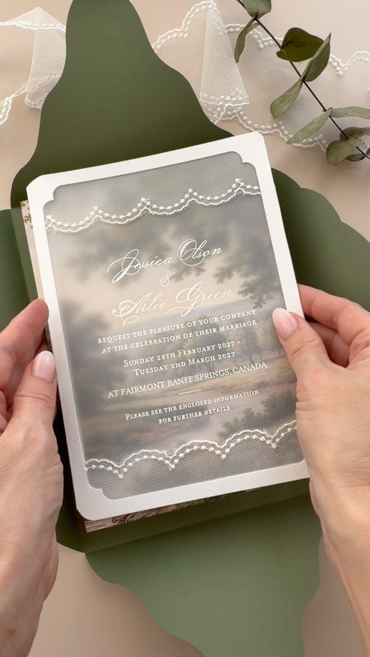 Wedding invitation held over olive green cardstock with lace and greenery