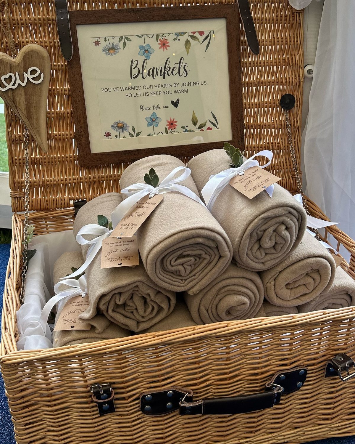 Rolled beige blankets with white ribbons in a wicker basket with a sign.
