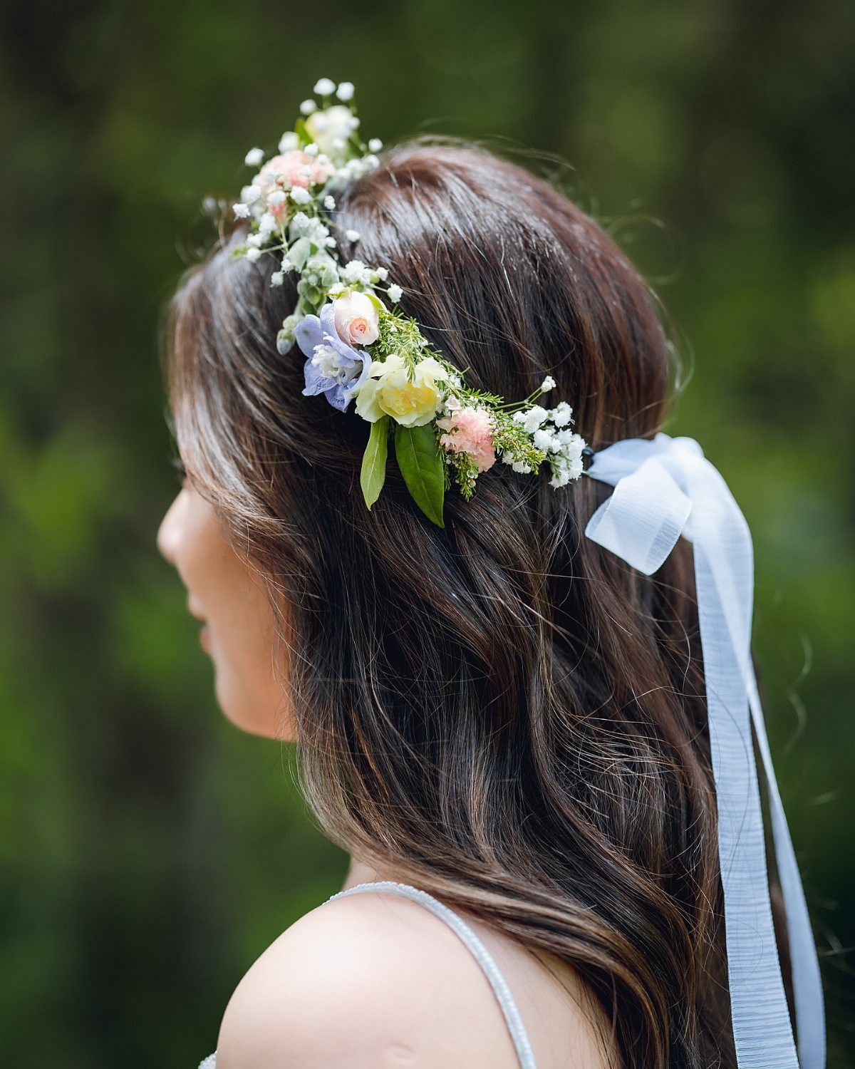 Woman wearing a delicate floral crown with pink and purple flowers and white ribbon.