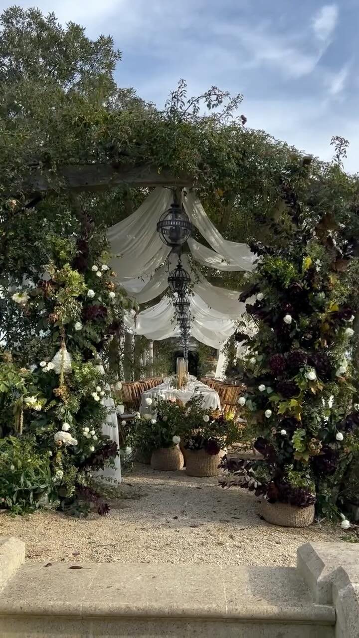 Floral wedding arbor with white fabric and lanterns in a lush forest setting