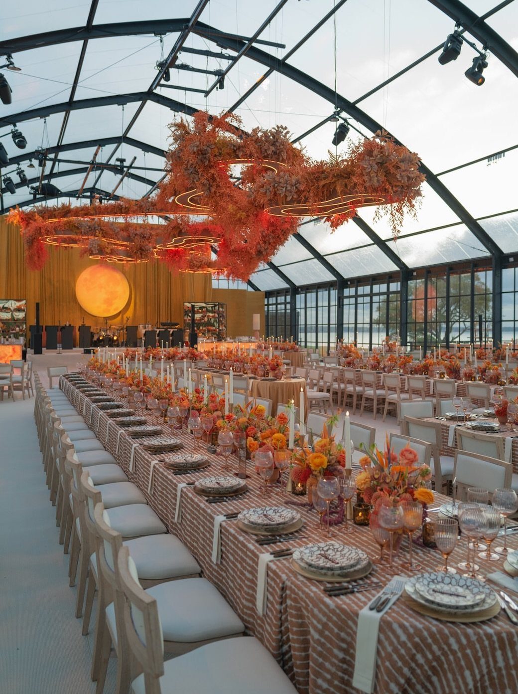 Long banquet table with autumn floral arrangements under hanging red fall leaves.