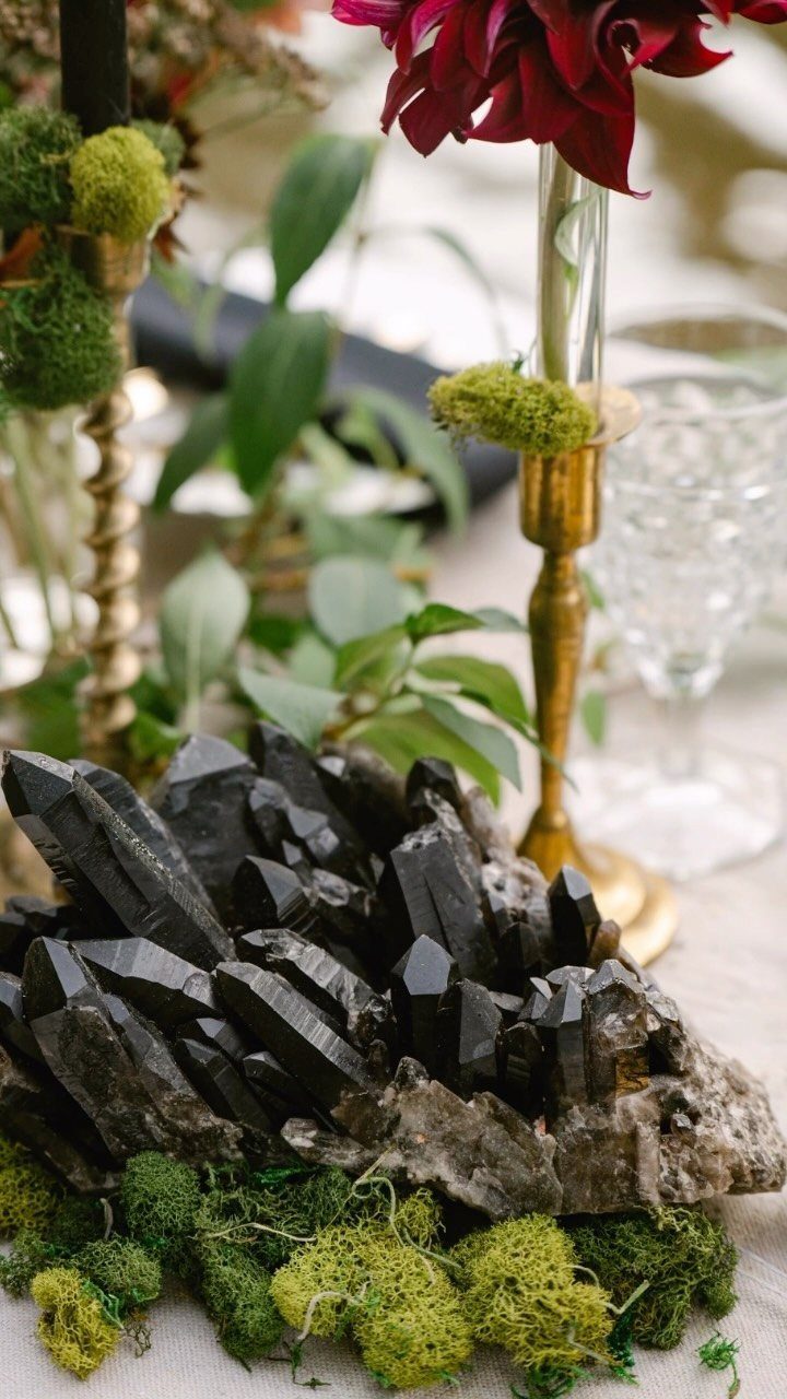 Dark smoky quartz crystals on green moss with gold accents and red flowers.