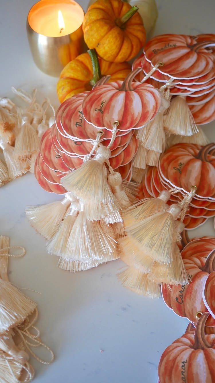 Small orange pumpkins and pumpkin-shaped place cards with tassels next to a lit candle.