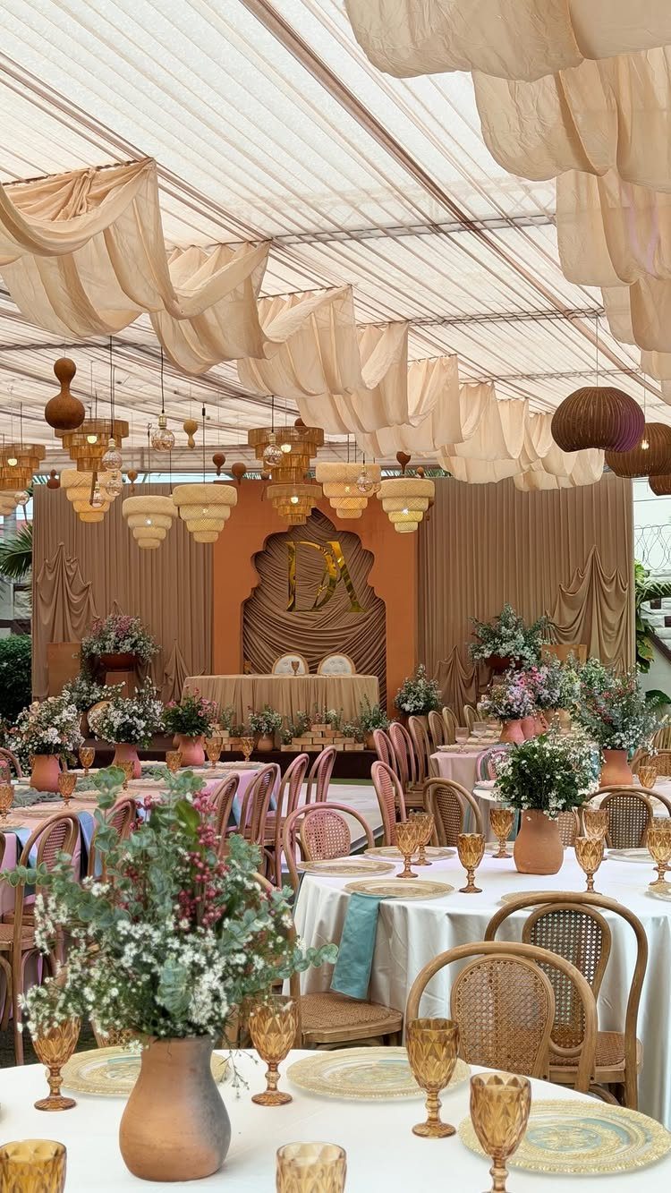 Terracotta vases and amber glassware on white tables with rattan chairs and fabric draping.