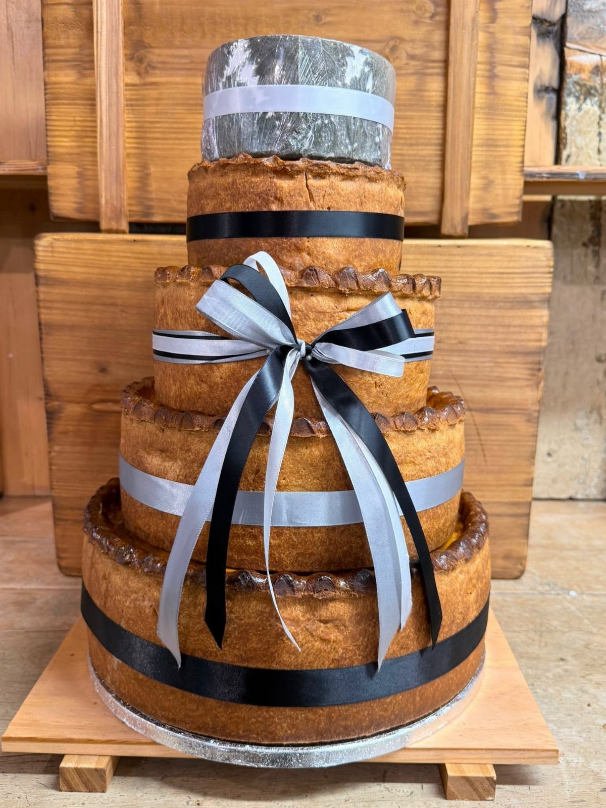 Tiered savory pie cake decorated with ribbons and topped with a cheese wheel.