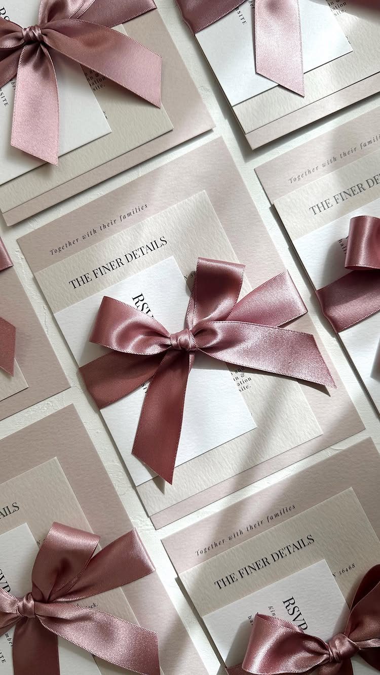 Wedding invitations with beige and white cards tied with mauve satin ribbons.