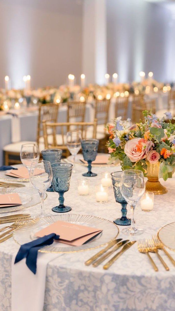 Wedding table setting with light blue linens, gold cutlery, and blue glassware.