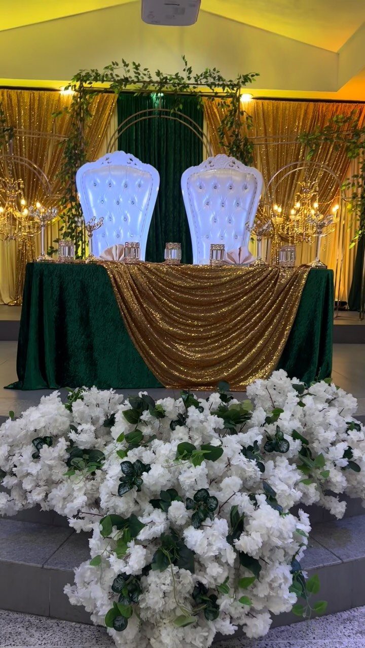 Emerald green and gold wedding table setup with white ornate chairs and flowers