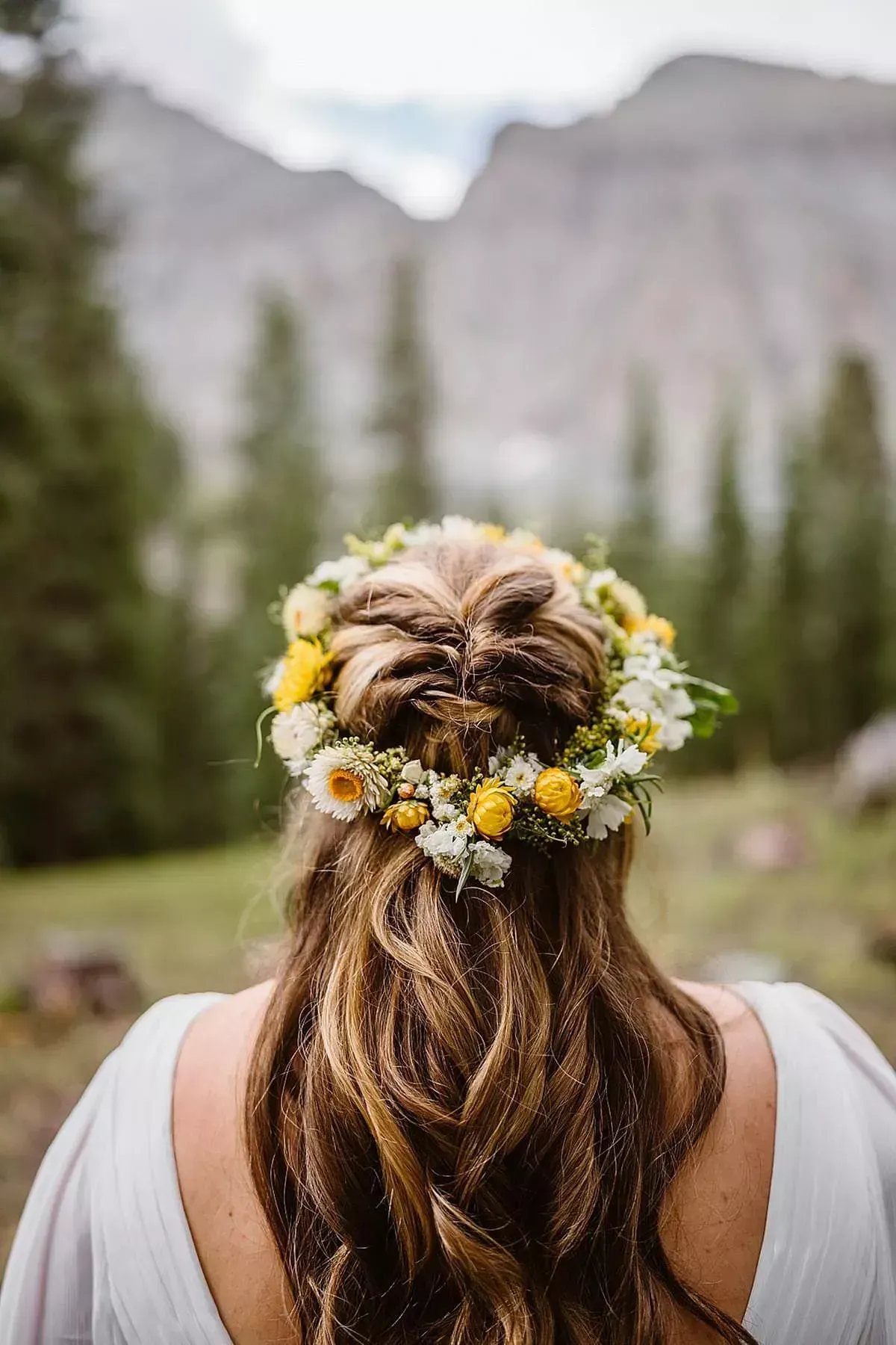 Woman with wavy brown hair wearing a yellow and white floral crown outdoors.