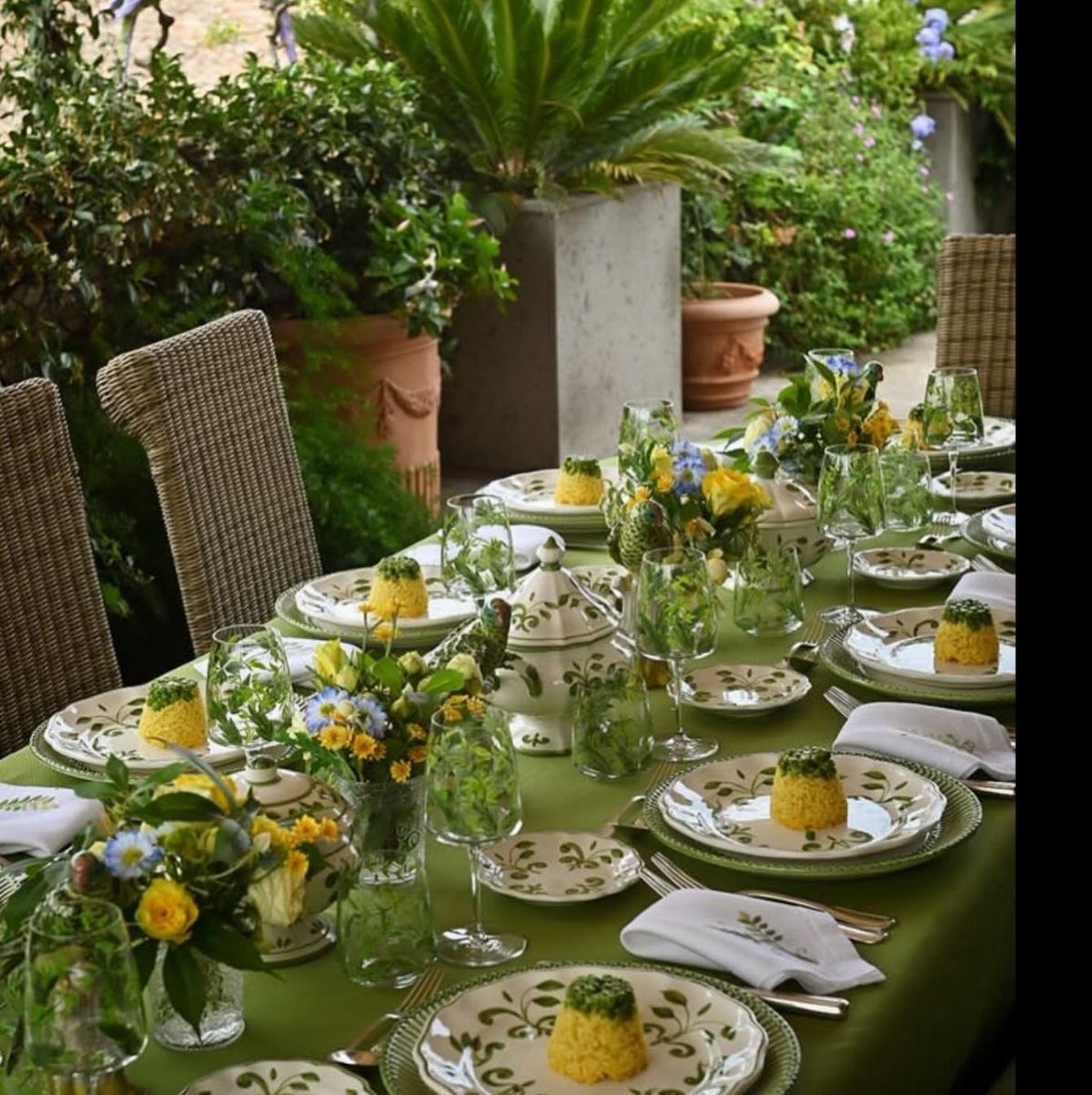 Outdoor dining table with green tablecloth, yellow food, and yellow floral centerpieces.
