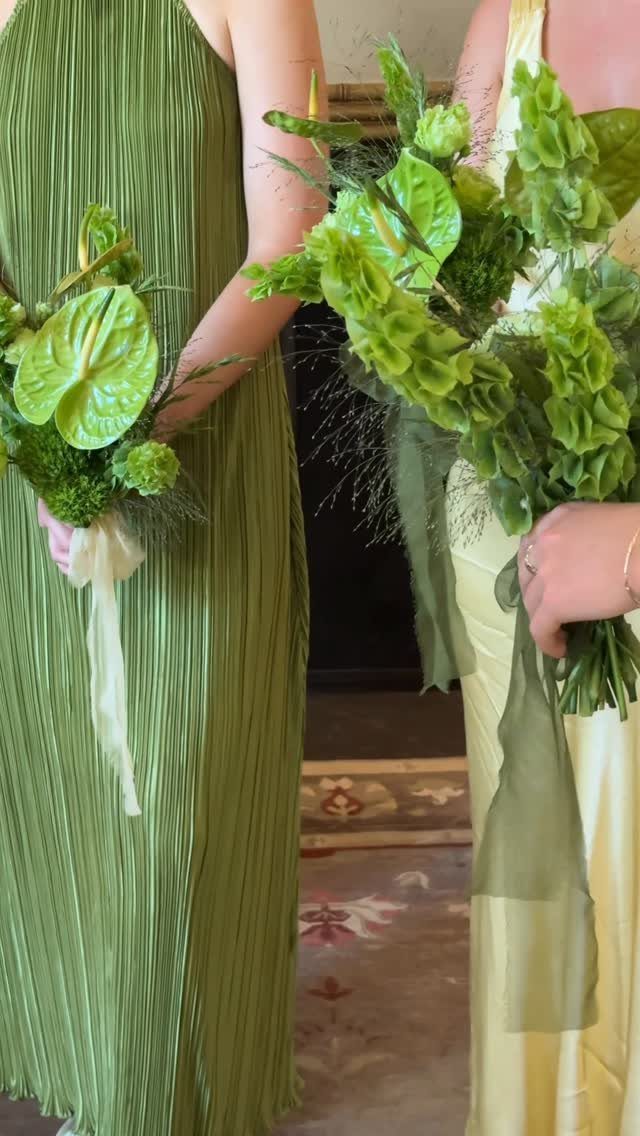 Two women in olive green and pale yellow gowns holding green floral bouquets.
